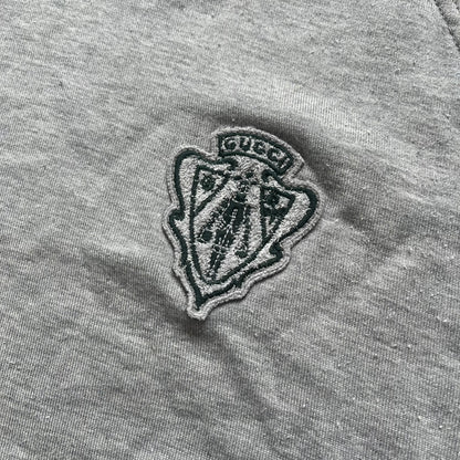 Gucci Gray Crest Patch Sherry Line Zip-Up Hoodie is a lightweight gray zip hoodie made in Italy. The chest features a crest patch with Gucci logo, while the bottom hem includes the green and red Web (Sherry Line) detail. The drawstrings have metal aglets engraved with Gucci branding.