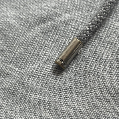Gucci Gray Crest Patch Sherry Line Zip-Up Hoodie is a lightweight gray zip hoodie made in Italy. The chest features a crest patch with Gucci logo, while the bottom hem includes the green and red Web (Sherry Line) detail. The drawstrings have metal aglets engraved with Gucci branding.