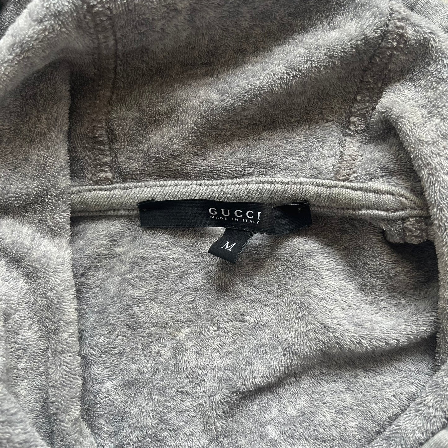 Gucci Gray Crest Patch Sherry Line Zip-Up Hoodie is a lightweight gray zip hoodie made in Italy. The chest features a crest patch with Gucci logo, while the bottom hem includes the green and red Web (Sherry Line) detail. The drawstrings have metal aglets engraved with Gucci branding.