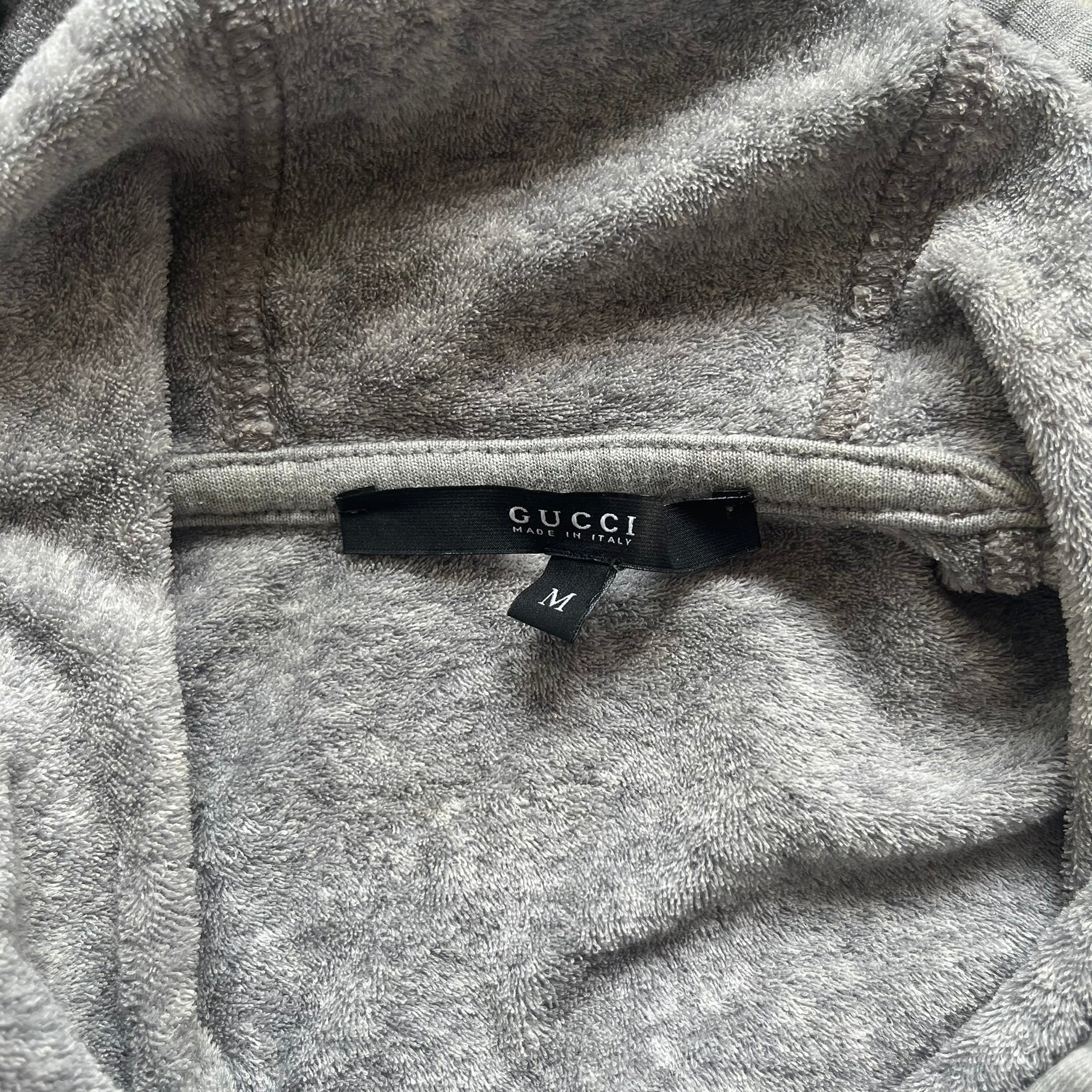 Gucci Gray Crest Patch Sherry Line Zip-Up Hoodie is a lightweight gray zip hoodie made in Italy. The chest features a crest patch with Gucci logo, while the bottom hem includes the green and red Web (Sherry Line) detail. The drawstrings have metal aglets engraved with Gucci branding.