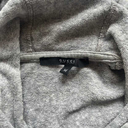 Gucci Gray Crest Patch Sherry Line Zip-Up Hoodie is a lightweight gray zip hoodie made in Italy. The chest features a crest patch with Gucci logo, while the bottom hem includes the green and red Web (Sherry Line) detail. The drawstrings have metal aglets engraved with Gucci branding.