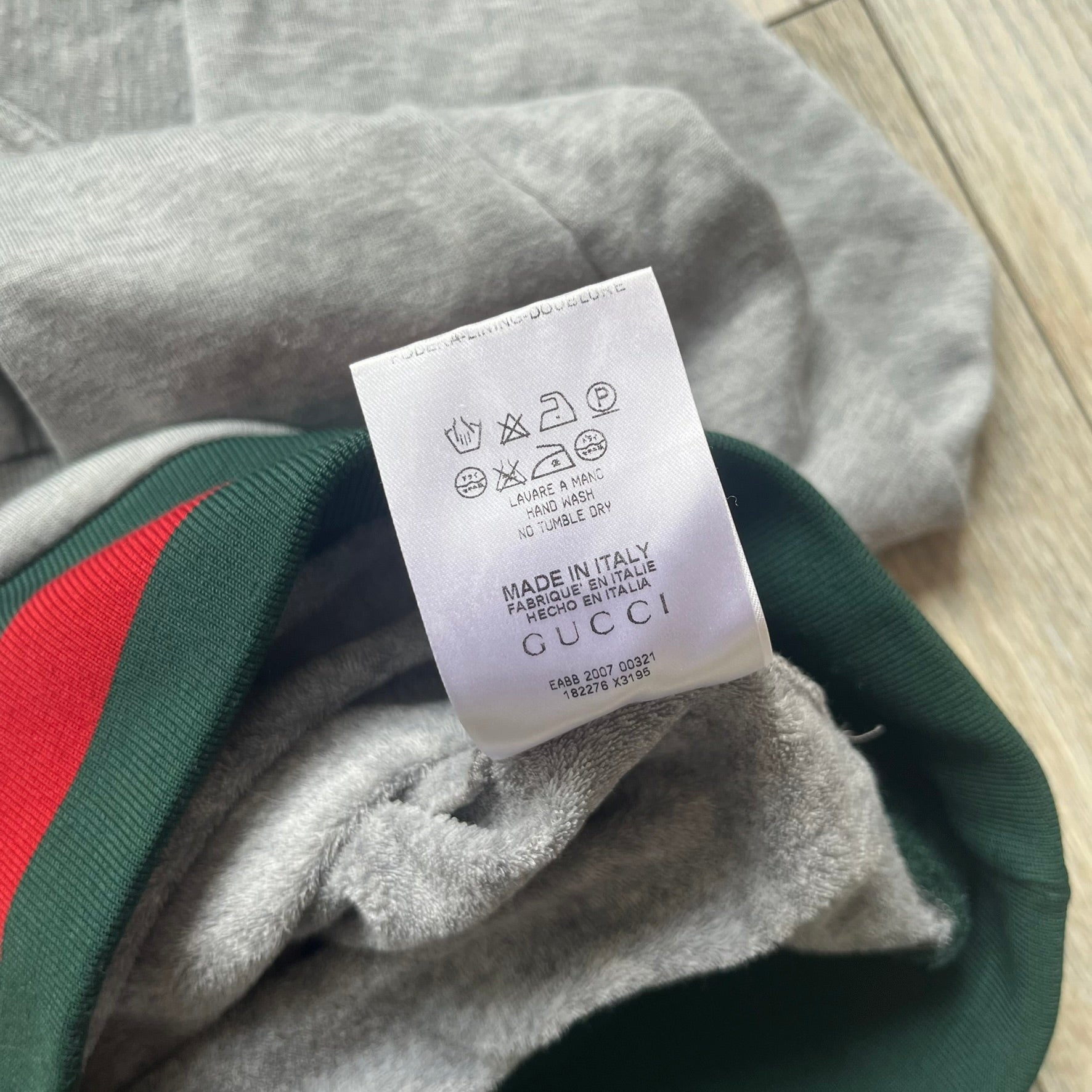 Gucci Gray Crest Patch Sherry Line Zip-Up Hoodie is a lightweight gray zip hoodie made in Italy. The chest features a crest patch with Gucci logo, while the bottom hem includes the green and red Web (Sherry Line) detail. The drawstrings have metal aglets engraved with Gucci branding.