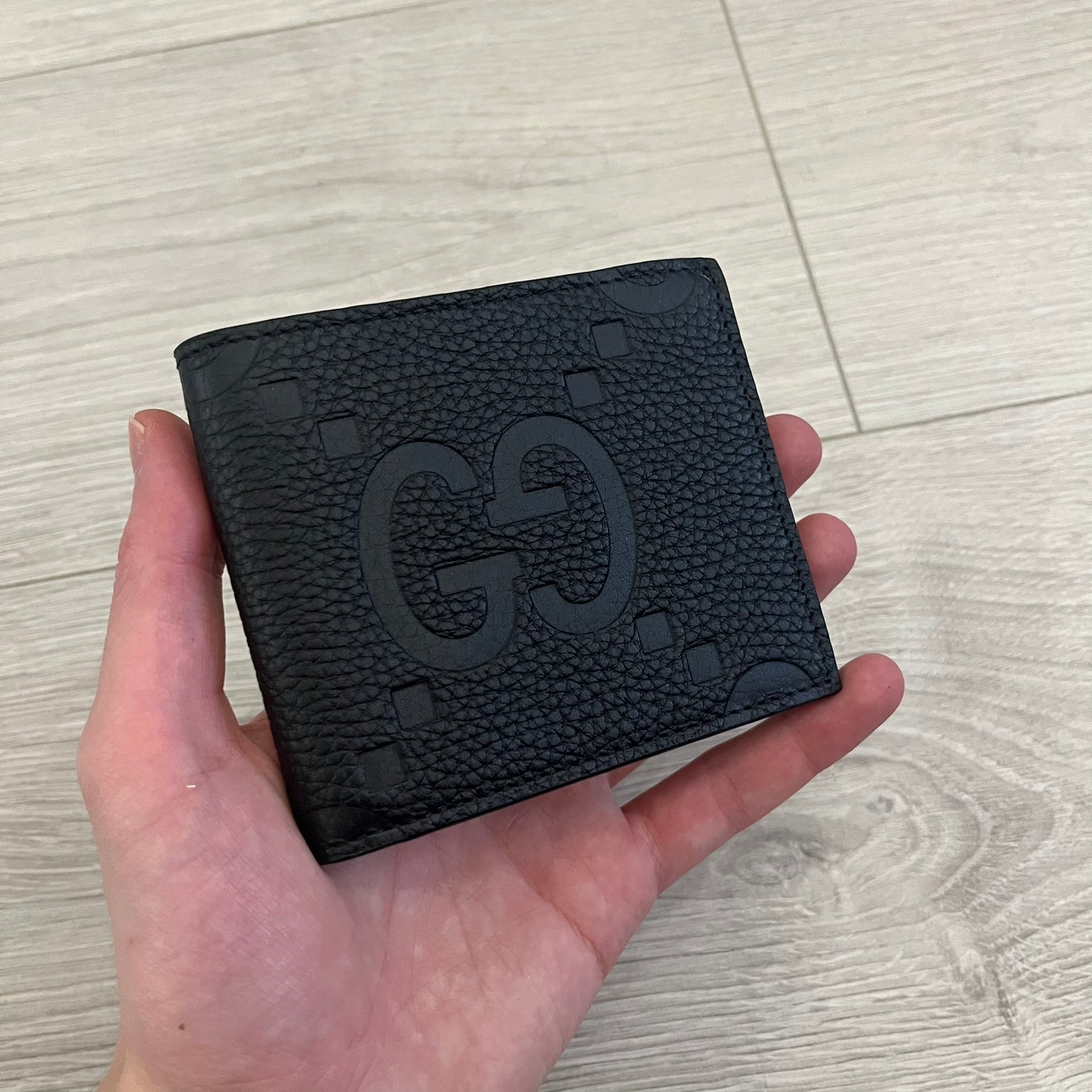 Gucci Jumbo GG Bi-Fold Leather Wallet in black calfskin, featuring the brand’s iconic debossed Jumbo GG logo. This Italian-made wallet offers eight card slots, two bill compartments, and a bi-fold design for organized storage. Finished with grained leather and a moiré lining.