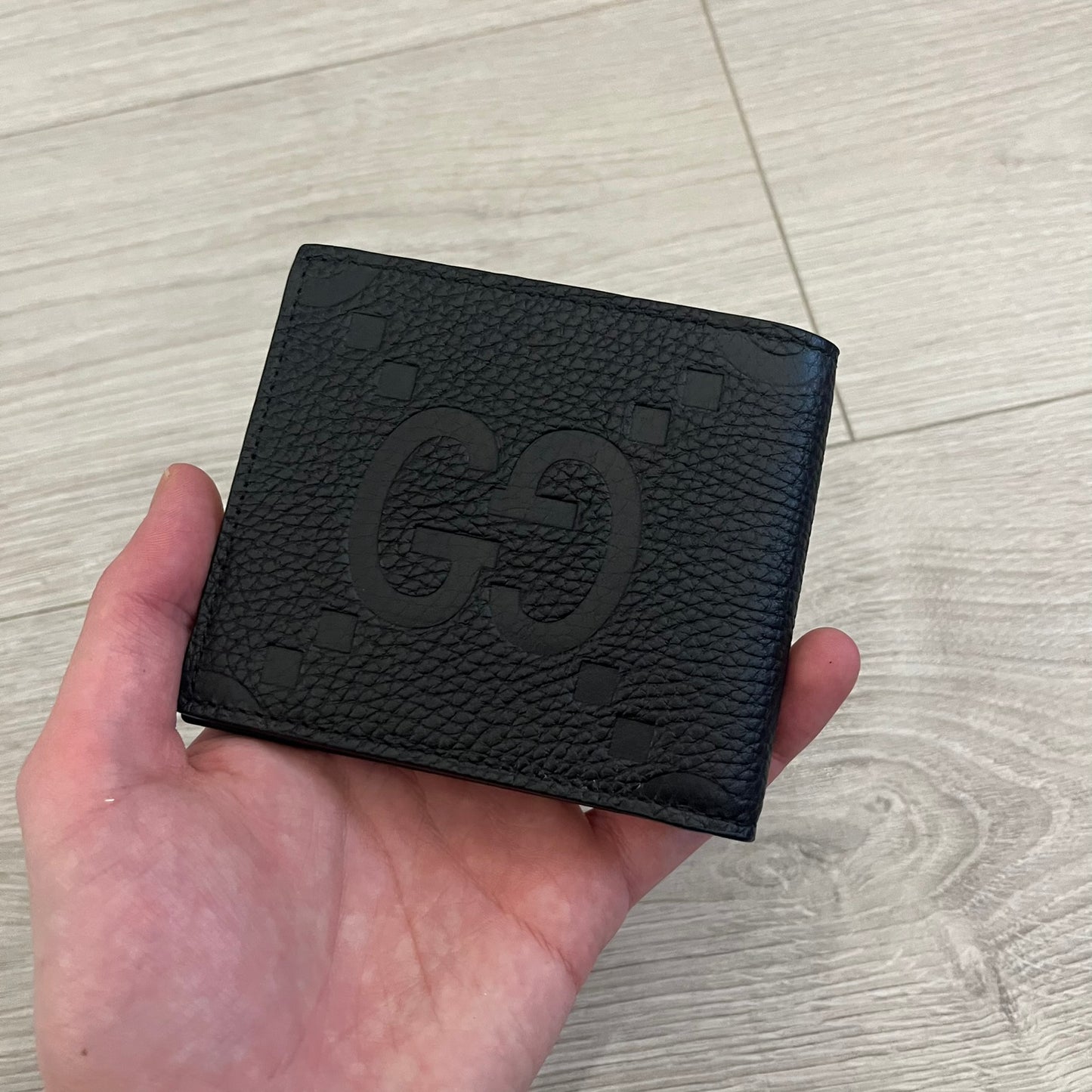 Gucci Jumbo GG Bi-Fold Leather Wallet in black calfskin, featuring the brand’s iconic debossed Jumbo GG logo. This Italian-made wallet offers eight card slots, two bill compartments, and a bi-fold design for organized storage. Finished with grained leather and a moiré lining.