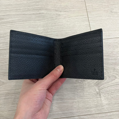 Gucci Jumbo GG Bi-Fold Leather Wallet in black calfskin, featuring the brand’s iconic debossed Jumbo GG logo. This Italian-made wallet offers eight card slots, two bill compartments, and a bi-fold design for organized storage. Finished with grained leather and a moiré lining.
