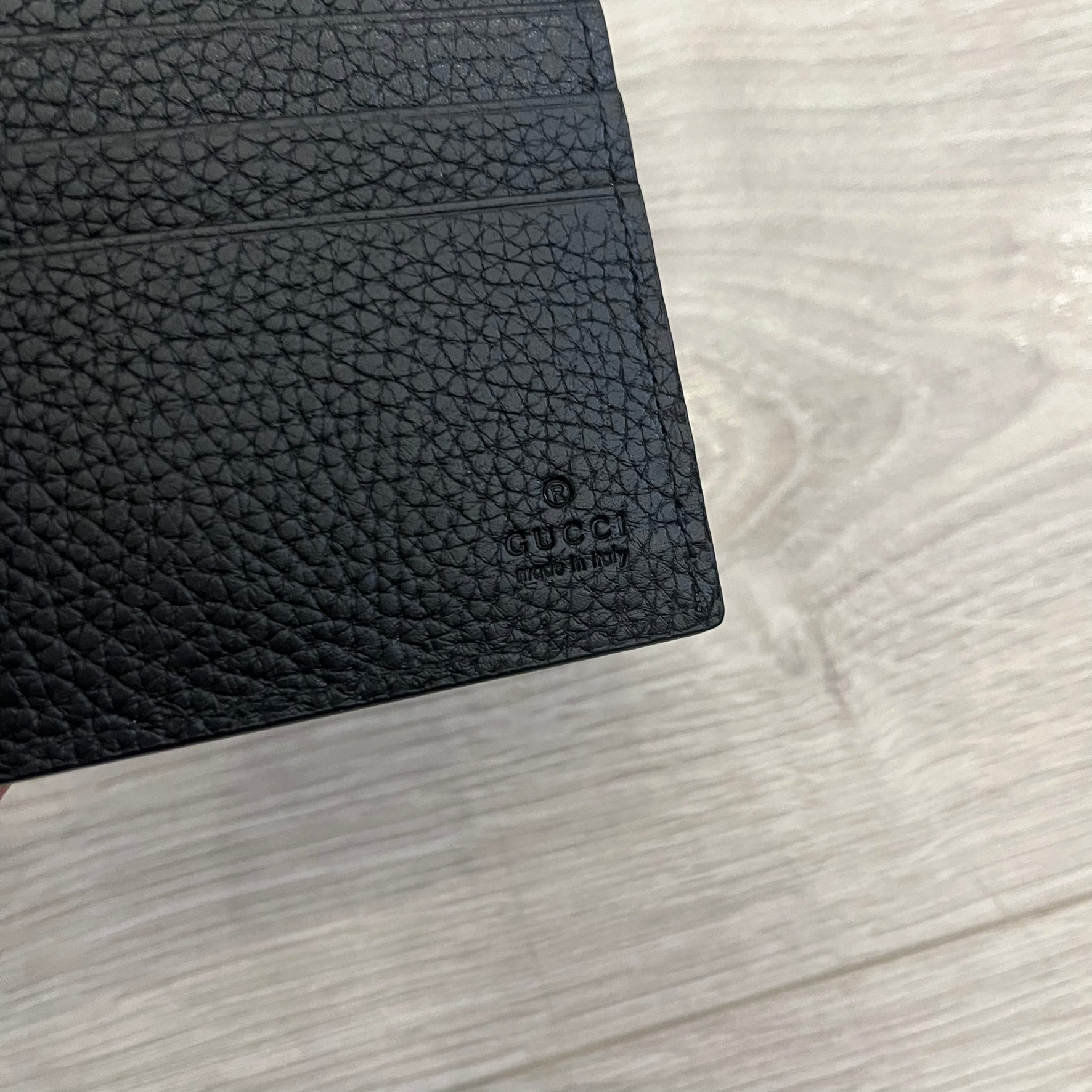Gucci Jumbo GG Bi-Fold Leather Wallet in black calfskin, featuring the brand’s iconic debossed Jumbo GG logo. This Italian-made wallet offers eight card slots, two bill compartments, and a bi-fold design for organized storage. Finished with grained leather and a moiré lining.