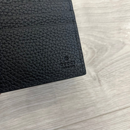 Gucci Jumbo GG Bi-Fold Leather Wallet in black calfskin, featuring the brand’s iconic debossed Jumbo GG logo. This Italian-made wallet offers eight card slots, two bill compartments, and a bi-fold design for organized storage. Finished with grained leather and a moiré lining.