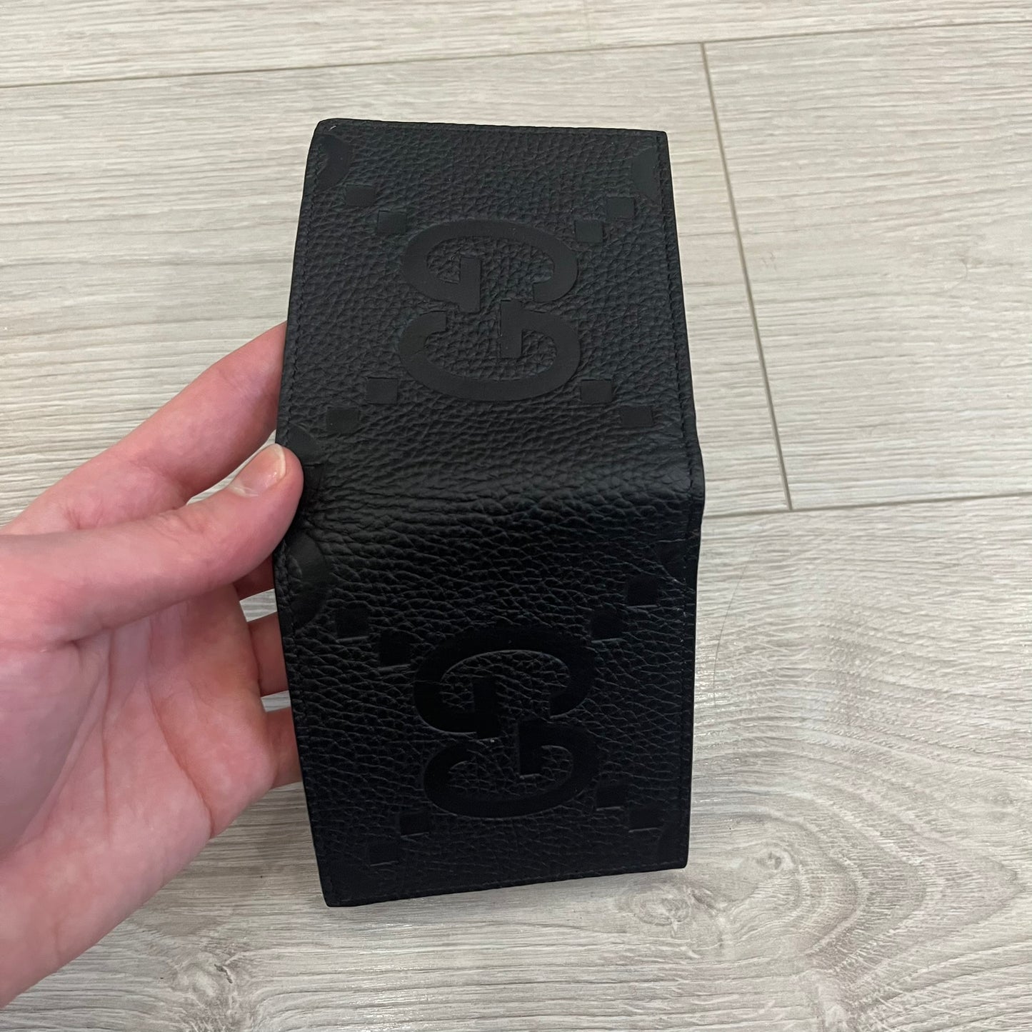 Gucci Jumbo GG Bi-Fold Leather Wallet in black calfskin, featuring the brand’s iconic debossed Jumbo GG logo. This Italian-made wallet offers eight card slots, two bill compartments, and a bi-fold design for organized storage. Finished with grained leather and a moiré lining.