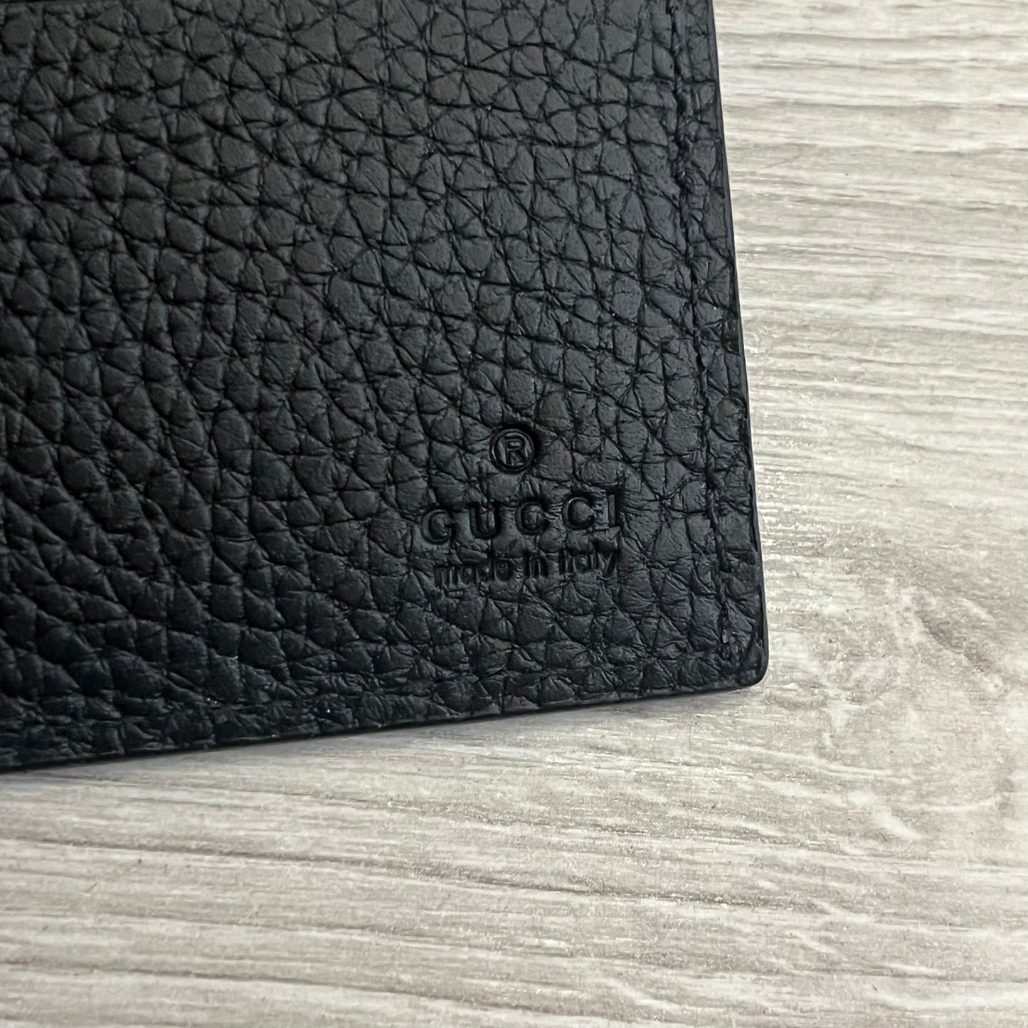 Gucci Jumbo GG Bi-Fold Leather Wallet in black calfskin, featuring the brand’s iconic debossed Jumbo GG logo. This Italian-made wallet offers eight card slots, two bill compartments, and a bi-fold design for organized storage. Finished with grained leather and a moiré lining.