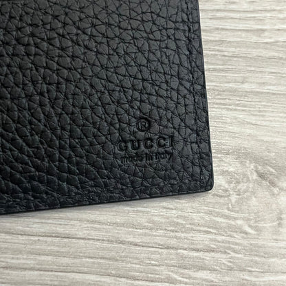 Gucci Jumbo GG Bi-Fold Leather Wallet in black calfskin, featuring the brand’s iconic debossed Jumbo GG logo. This Italian-made wallet offers eight card slots, two bill compartments, and a bi-fold design for organized storage. Finished with grained leather and a moiré lining.