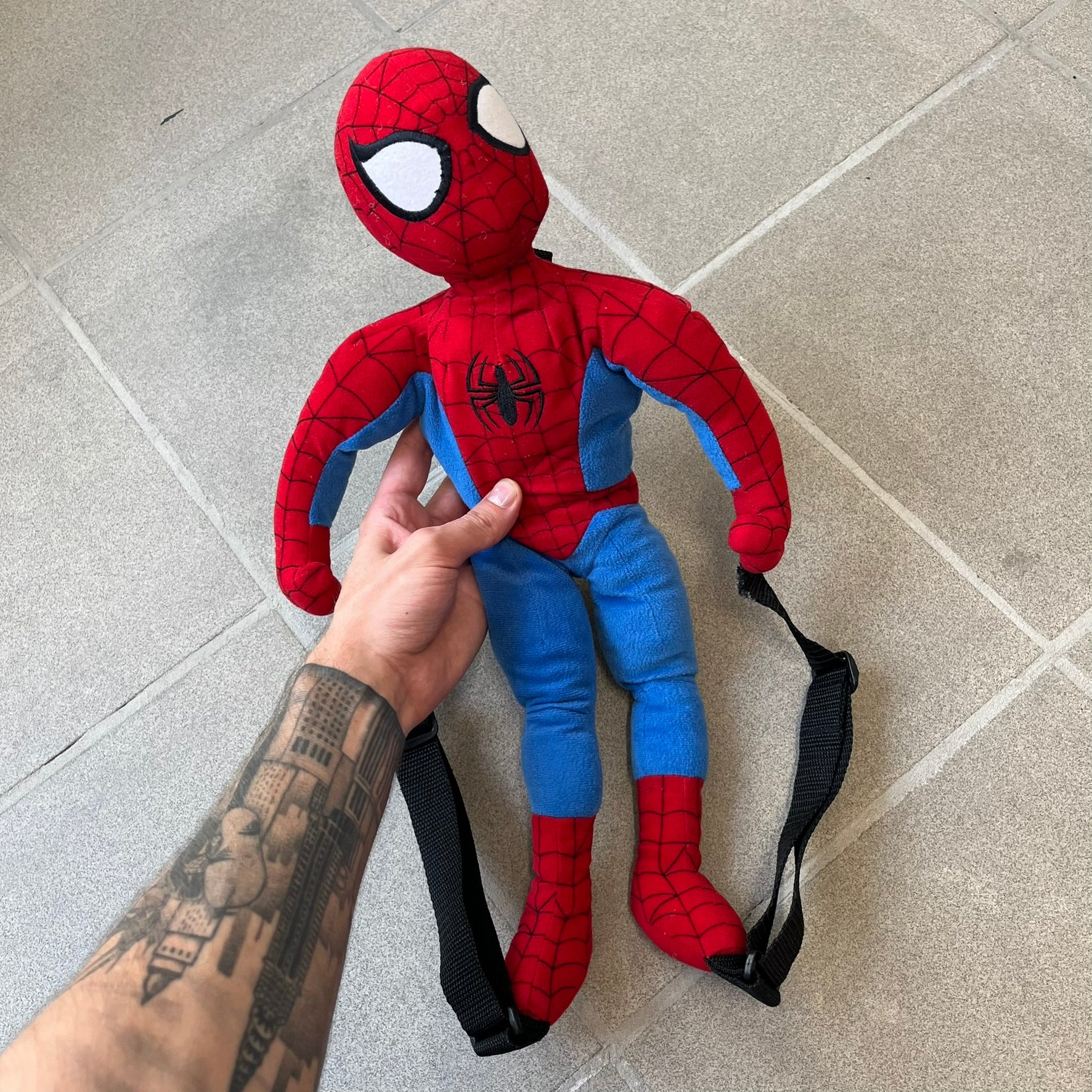 H&M x Marvel 2006 Spider-Man Backpack is a red and blue backpack shaped like Spider-Man in his signature costume. The design features embroidered eye details and an embroidered spider logo on the chest. It has a compact back pocket and straps connected from the character’s hands to the legs. Includes 2006 H&M x Marvel licensing details.

