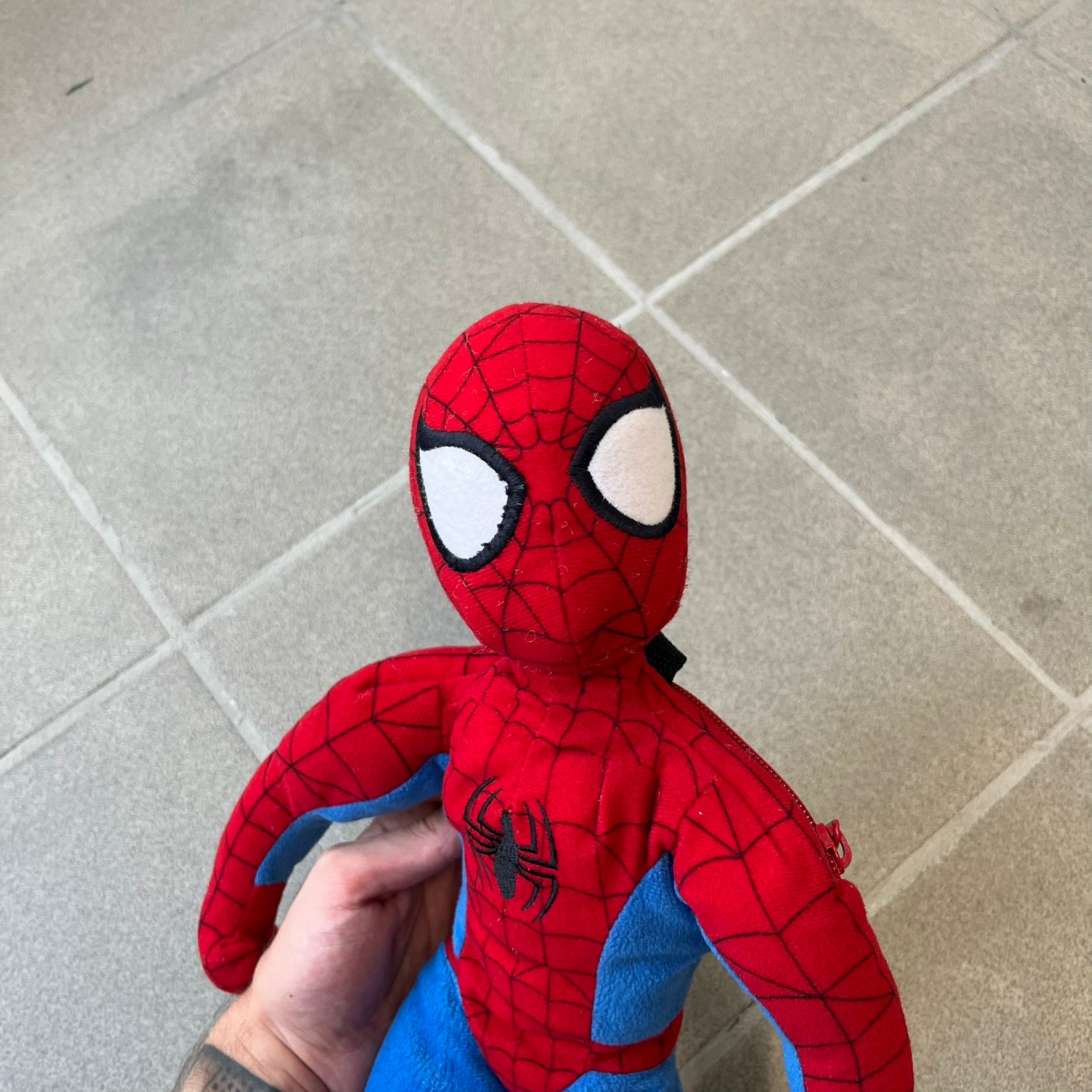 H&M x Marvel 2006 Spider-Man Backpack is a red and blue backpack shaped like Spider-Man in his signature costume. The design features embroidered eye details and an embroidered spider logo on the chest. It has a compact back pocket and straps connected from the character’s hands to the legs. Includes 2006 H&M x Marvel licensing details.

