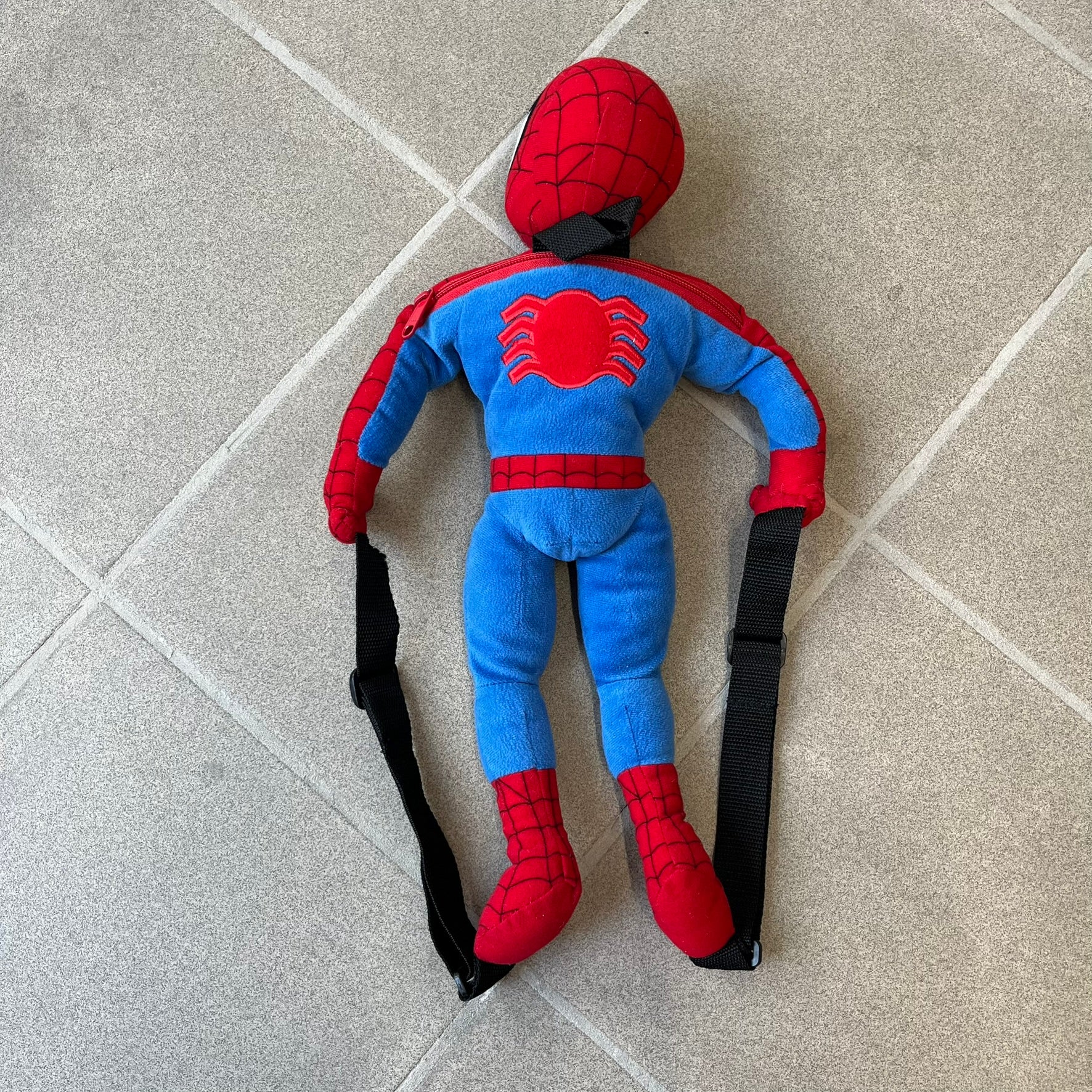 H&M x Marvel 2006 Spider-Man Backpack is a red and blue backpack shaped like Spider-Man in his signature costume. The design features embroidered eye details and an embroidered spider logo on the chest. It has a compact back pocket and straps connected from the character’s hands to the legs. Includes 2006 H&M x Marvel licensing details.
