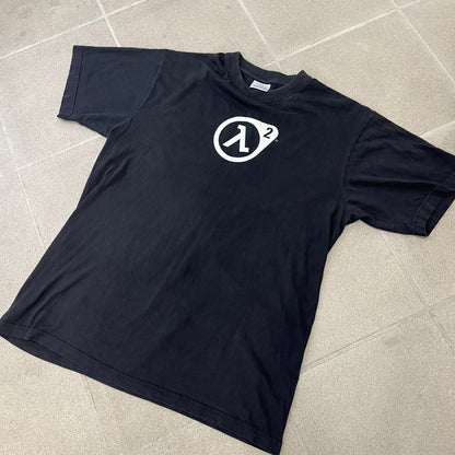 Half-Life 2 2000’s Lambda Black Tee is a black, 100% cotton T-shirt with a white Half-Life 2 logo on the front, showing the lambda symbol inside a circle with a “2” in the corner and a small TM mark beside it.