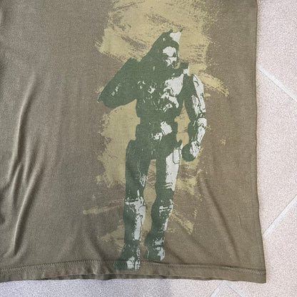 Halo 3 Finish the Fight 2006 Tee is a khaki, 100% cotton T-shirt with a green Master Chief graphic on the front against a lighter background. A Halo 3 logo is on one sleeve, and “Finish the Fight” text runs across the upper back. The neck tag is licensed for Xbox 360 and carries 2005 licensing on the other side.