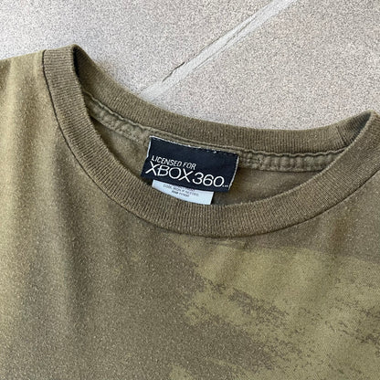 Halo 3 Finish the Fight 2006 Tee is a khaki, 100% cotton T-shirt with a green Master Chief graphic on the front against a lighter background. A Halo 3 logo is on one sleeve, and “Finish the Fight” text runs across the upper back. The neck tag is licensed for Xbox 360 and carries 2005 licensing on the other side.