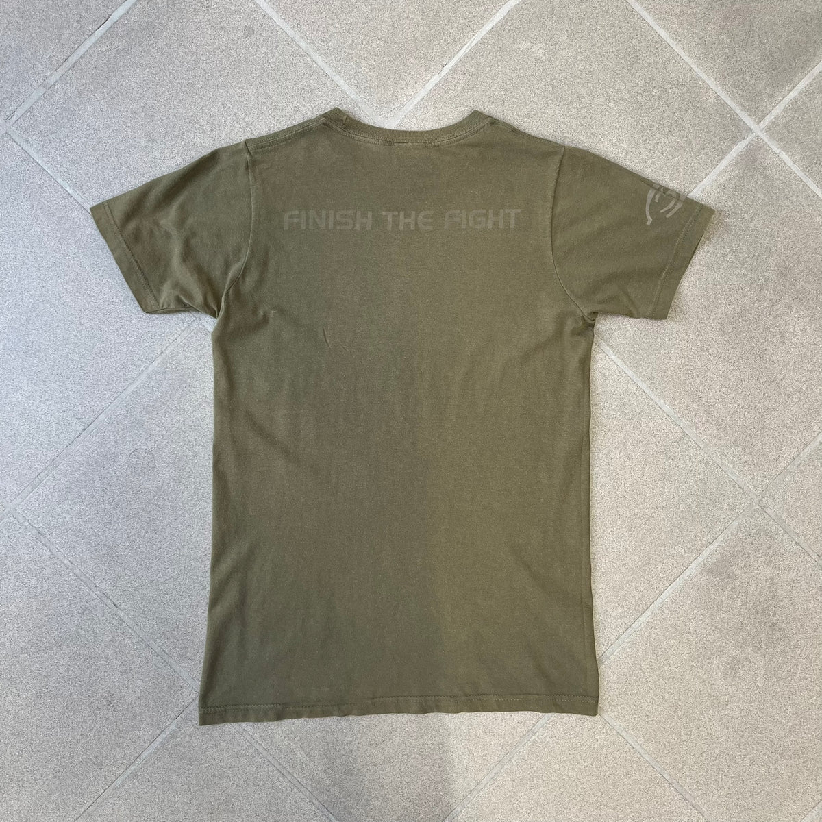 Halo 3 Finish the Fight 2006 Tee is a khaki, 100% cotton T-shirt with a green Master Chief graphic on the front against a lighter background. A Halo 3 logo is on one sleeve, and “Finish the Fight” text runs across the upper back. The neck tag is licensed for Xbox 360 and carries 2005 licensing on the other side.