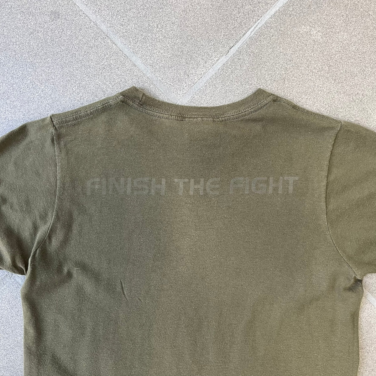 Halo 3 Finish the Fight 2006 Tee is a khaki, 100% cotton T-shirt with a green Master Chief graphic on the front against a lighter background. A Halo 3 logo is on one sleeve, and “Finish the Fight” text runs across the upper back. The neck tag is licensed for Xbox 360 and carries 2005 licensing on the other side.