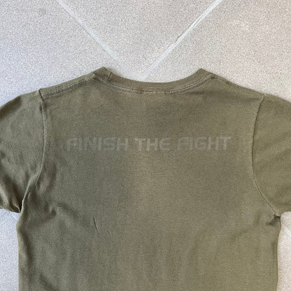 Halo 3 Finish the Fight 2006 Tee is a khaki, 100% cotton T-shirt with a green Master Chief graphic on the front against a lighter background. A Halo 3 logo is on one sleeve, and “Finish the Fight” text runs across the upper back. The neck tag is licensed for Xbox 360 and carries 2005 licensing on the other side.