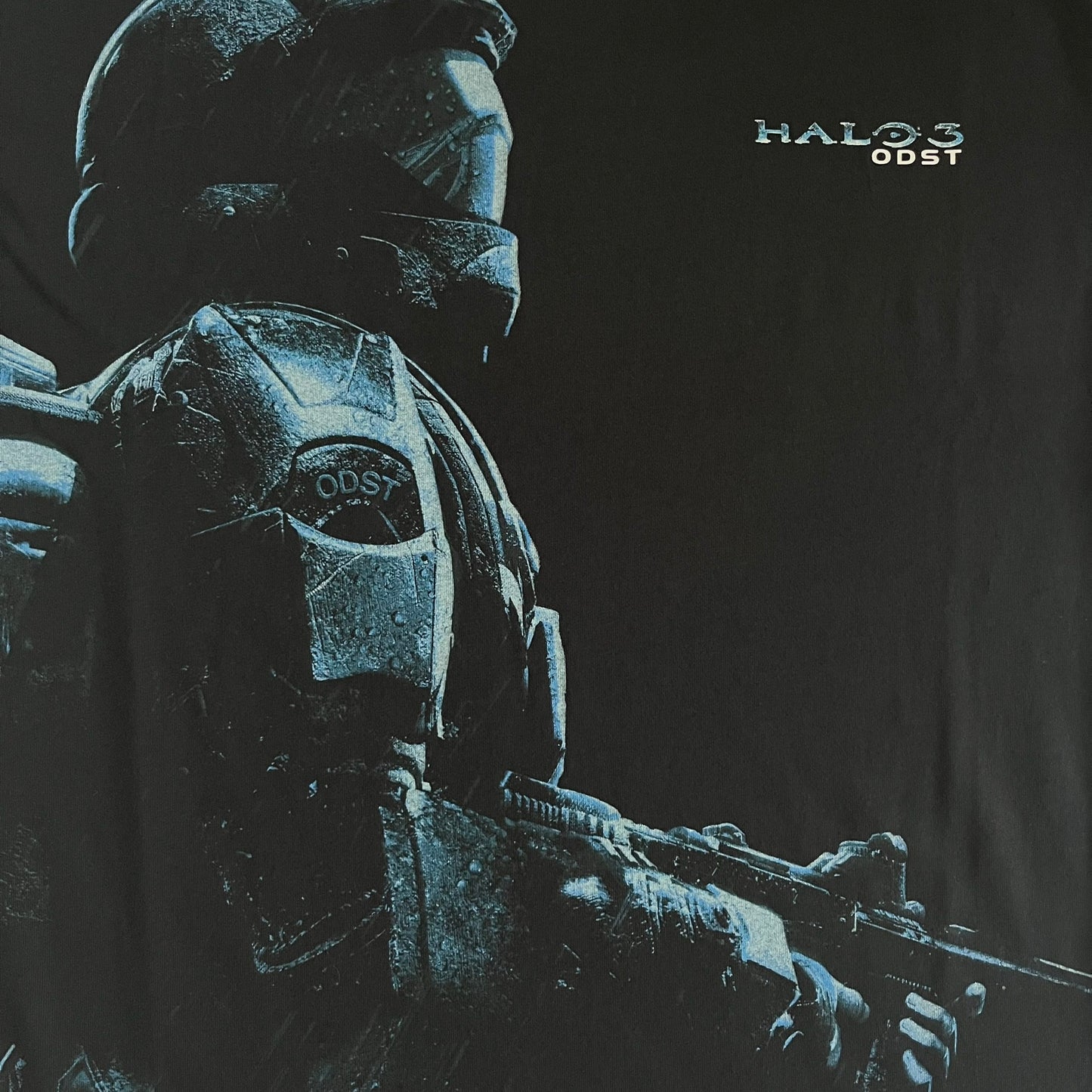 Black Halo 3: ODST Tee for Xbox 360 featuring a large blue Master Chief graphic on the front right and a small logo on the left chest. Made from high-quality cotton with Xbox 360 tags on the collar and a green one on the side. A super rare collectible for Halo fans.