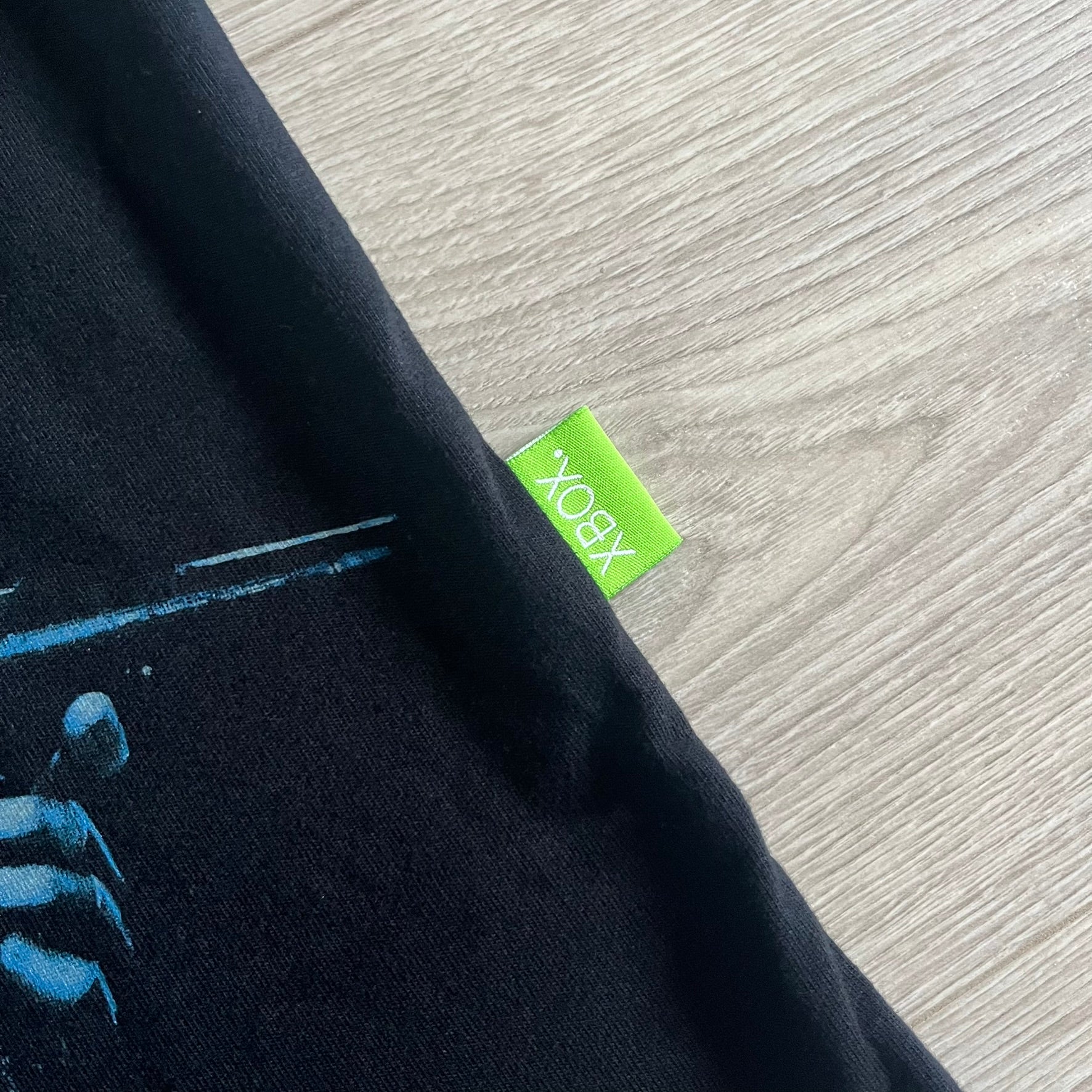 Black Halo 3: ODST Tee for Xbox 360 featuring a large blue Master Chief graphic on the front right and a small logo on the left chest. Made from high-quality cotton with Xbox 360 tags on the collar and a green one on the side. A super rare collectible for Halo fans.