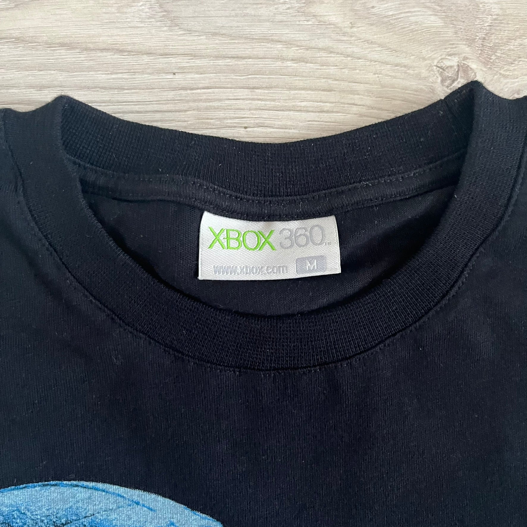Black Halo 3: ODST Tee for Xbox 360 featuring a large blue Master Chief graphic on the front right and a small logo on the left chest. Made from high-quality cotton with Xbox 360 tags on the collar and a green one on the side. A super rare collectible for Halo fans.