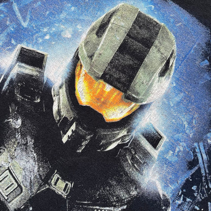 Halo 4 Master Chief 2012 Tee is a black graphic T-shirt featuring a large front print of Master Chief standing in front of a blue sci-fi style background. The design includes a detailed illustration of the character with a large Halo 4 logo printed below the graphic. The shirt has a 2012 Microsoft licensed neck tag.