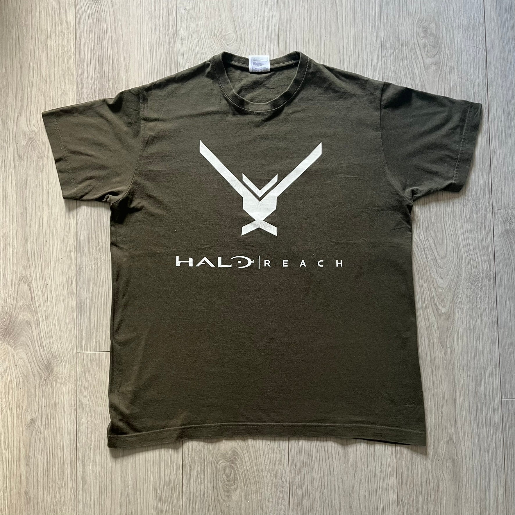Khaki Halo Reach tee on a Sol’s blank featuring the Noble Team emblem in white on the front and the Halo Reach logo beneath. Small Xbox 360 logo embroidered under the back collar. A classic collectible for fans of the iconic game series.