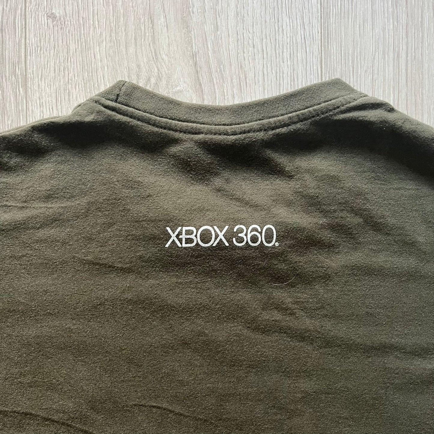 Khaki Halo Reach tee on a Sol’s blank featuring the Noble Team emblem in white on the front and the Halo Reach logo beneath. Small Xbox 360 logo embroidered under the back collar. A classic collectible for fans of the iconic game series.