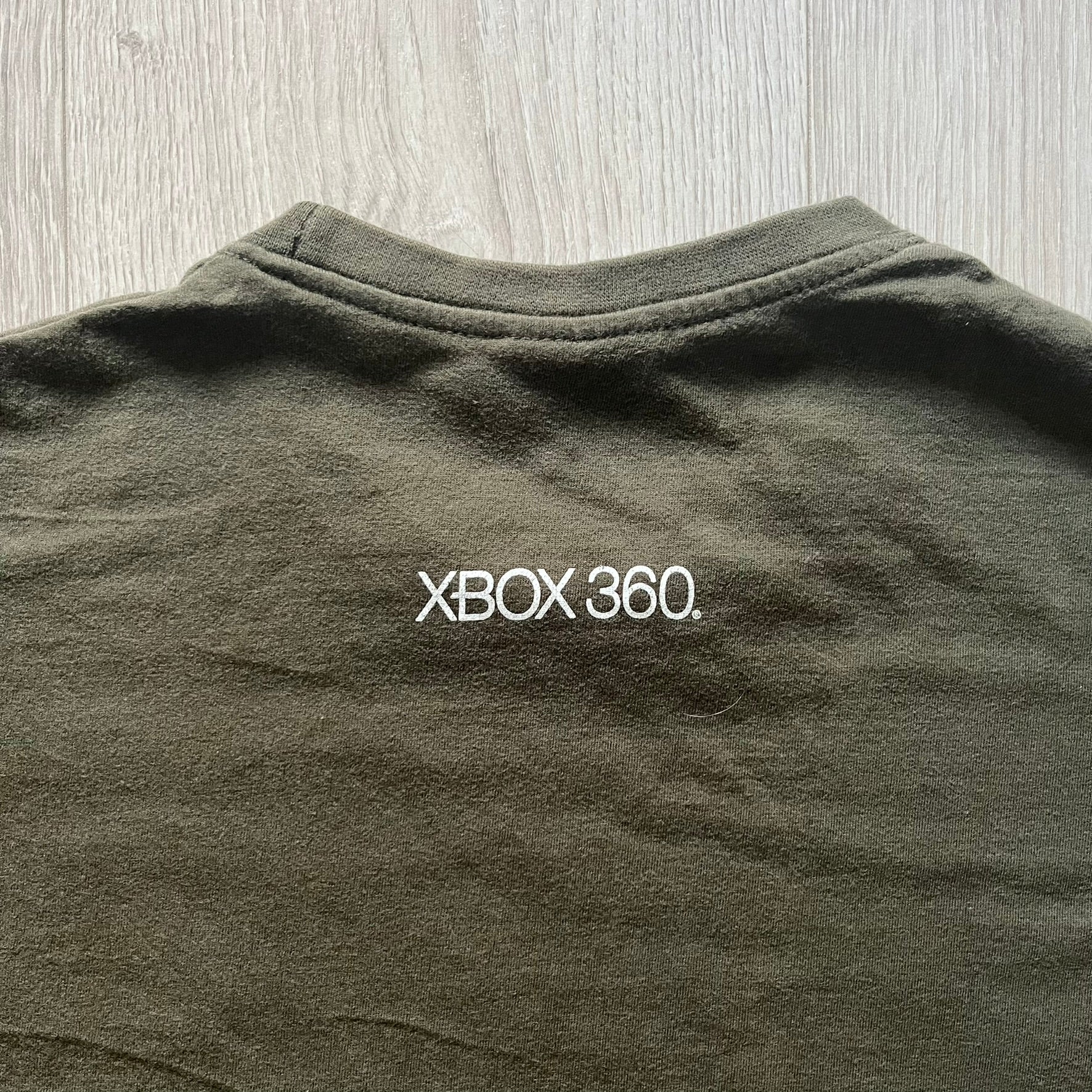 Khaki Halo Reach tee on a Sol’s blank featuring the Noble Team emblem in white on the front and the Halo Reach logo beneath. Small Xbox 360 logo embroidered under the back collar. A classic collectible for fans of the iconic game series.