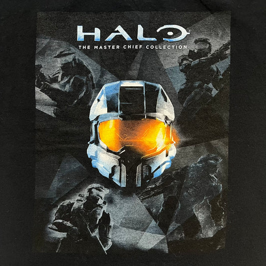Halo The Master Chief Collection 2010s Tee is a black short-sleeve T-shirt featuring a front graphic of Master Chief’s helmet with golden-orange visor, surrounded by smaller Master Chief figures. The back displays white “@GAMEDIGITAL” text, referencing the gaming merchandise website. This T-shirt was produced as part of official Halo merchandise in the 2010s.