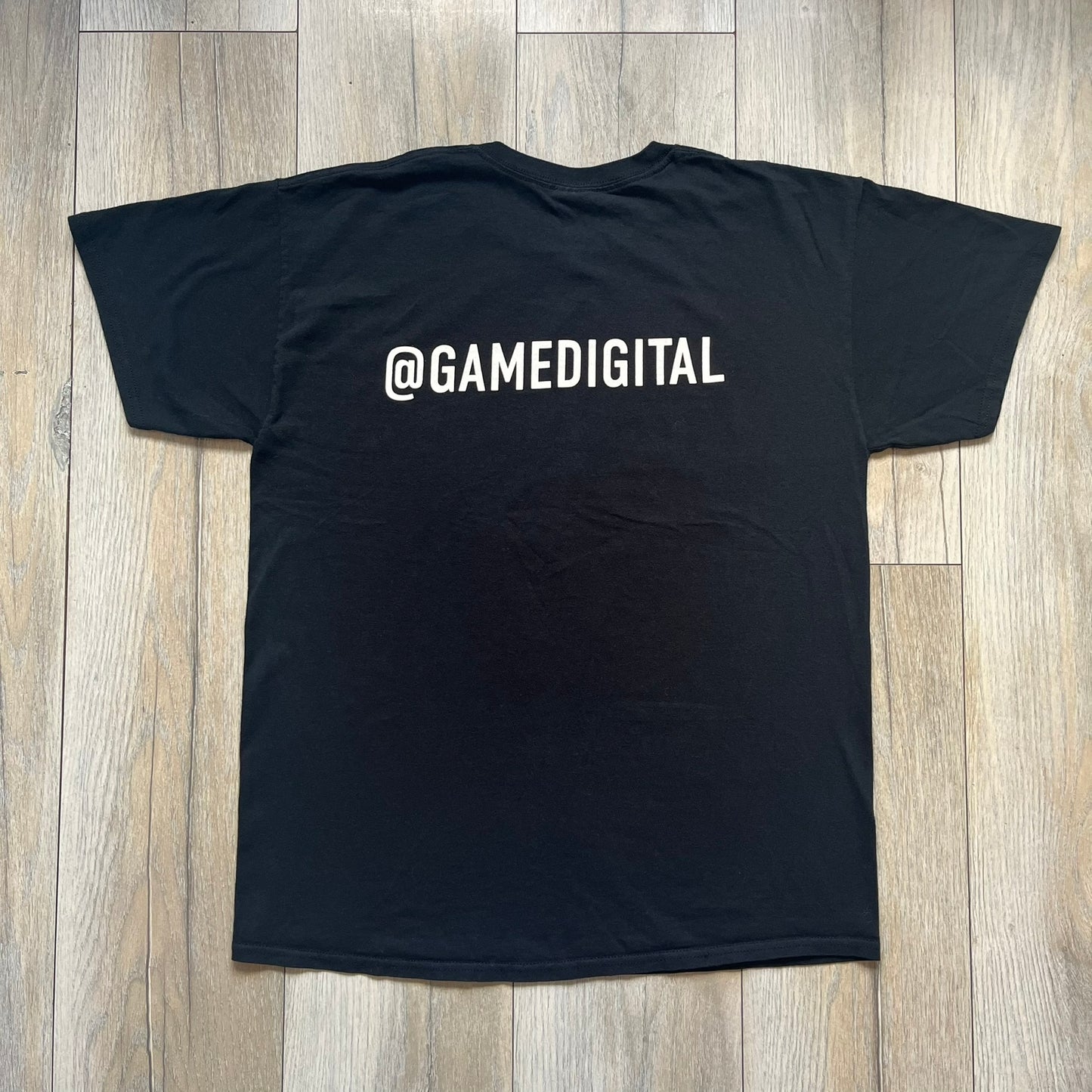 Halo The Master Chief Collection 2010s Tee is a black short-sleeve T-shirt featuring a front graphic of Master Chief’s helmet with golden-orange visor, surrounded by smaller Master Chief figures. The back displays white “@GAMEDIGITAL” text, referencing the gaming merchandise website. This T-shirt was produced as part of official Halo merchandise in the 2010s.