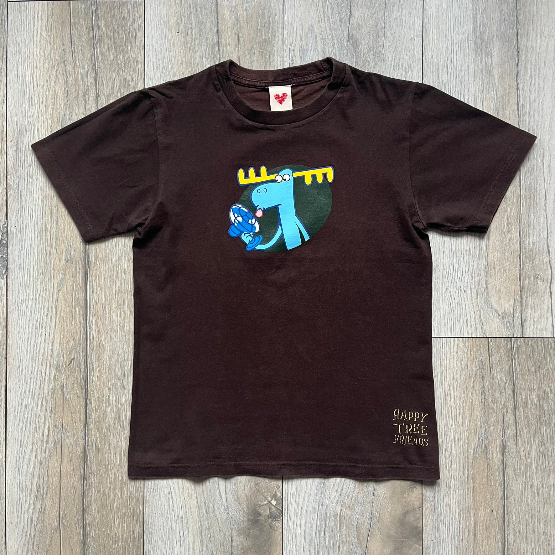Happy Tree Friends Lumpy Fan Brown Tee from 2005 is a brown T-shirt featuring Lumpy on the front holding and licking a fan. On the back, the same Lumpy graphic appears without the tongue, with visible blood on the fan and face. A small Happy Tree Friends logo is printed in the lower front corner, and the neck tag features a red heart detail.