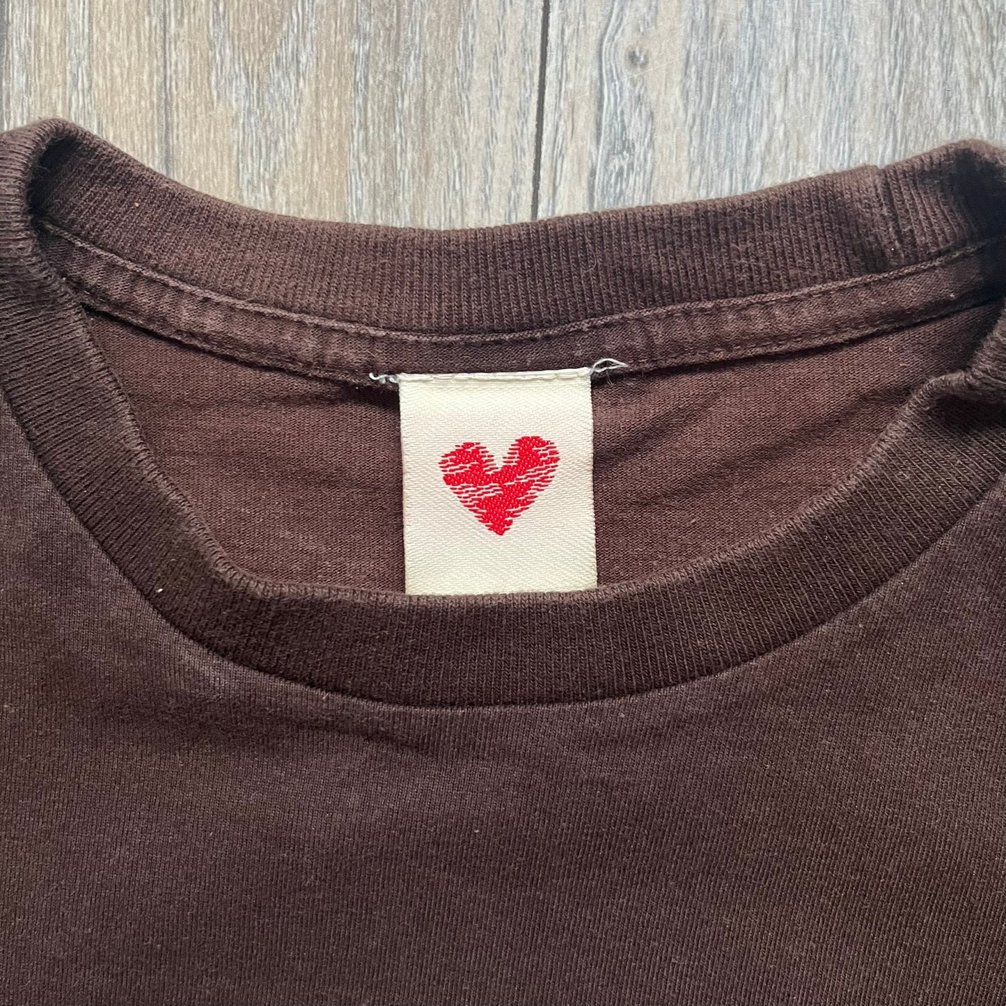 Happy Tree Friends Lumpy Fan Brown Tee from 2005 is a brown T-shirt featuring Lumpy on the front holding and licking a fan. On the back, the same Lumpy graphic appears without the tongue, with visible blood on the fan and face. A small Happy Tree Friends logo is printed in the lower front corner, and the neck tag features a red heart detail.