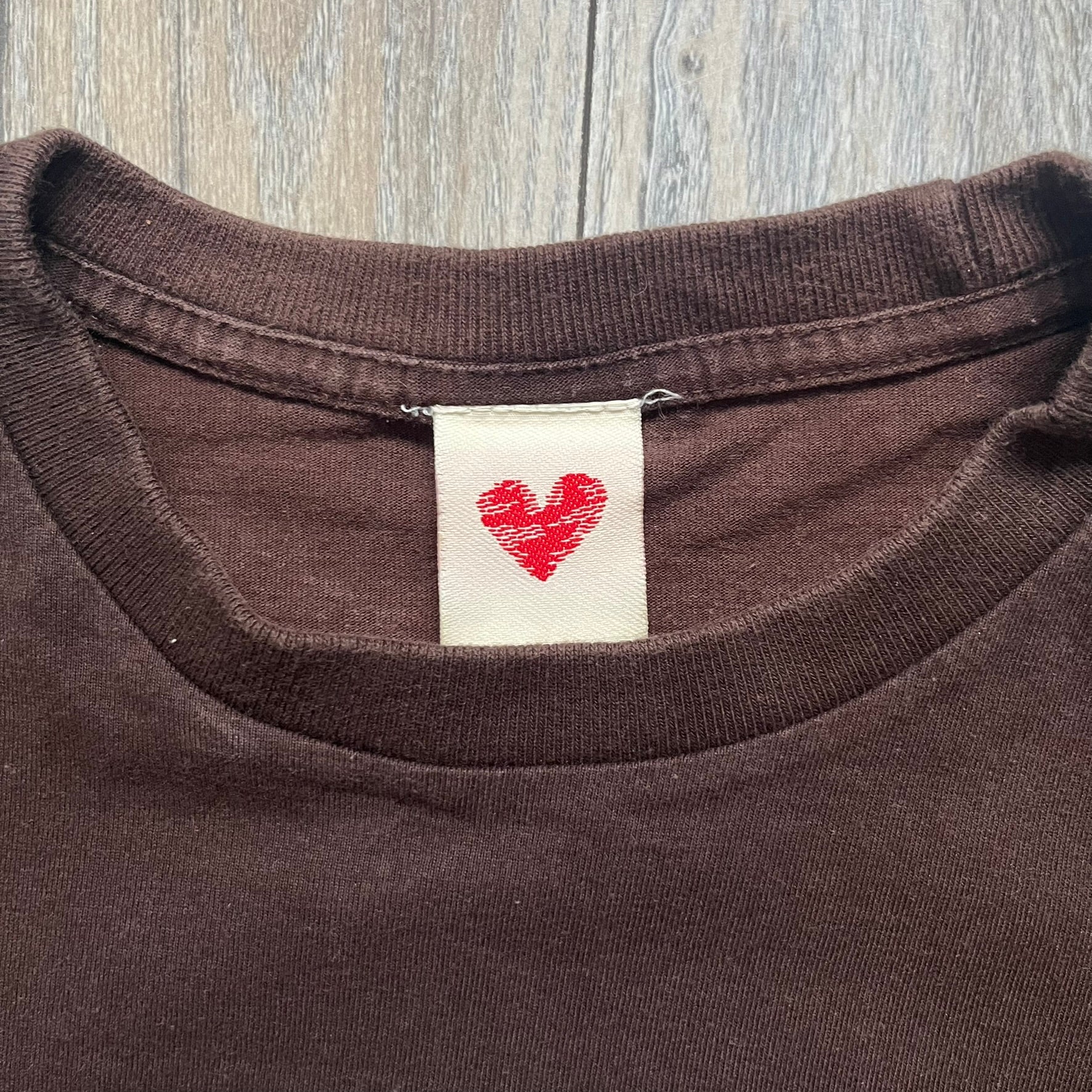 Happy Tree Friends Lumpy Fan Brown Tee from 2005 is a brown T-shirt featuring Lumpy on the front holding and licking a fan. On the back, the same Lumpy graphic appears without the tongue, with visible blood on the fan and face. A small Happy Tree Friends logo is printed in the lower front corner, and the neck tag features a red heart detail.