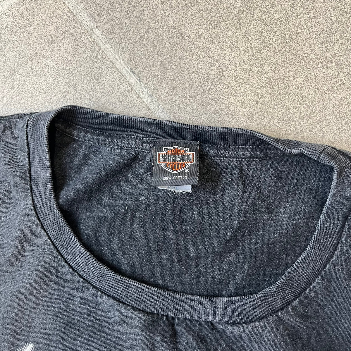 Harley-Davidson 2000's Eagle Black Tee features a boxy black T-shirt with a front graphic of an eagle's head alongside a Harley-Davidson logo. Purple and white “Harley Davidson” text and “Thunderstrikes” graphics surround the design. The back has a large white and grey graphic of a flying eagle with Harley-Davidson text underneath.
