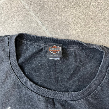 Harley-Davidson 2000's Eagle Black Tee features a boxy black T-shirt with a front graphic of an eagle's head alongside a Harley-Davidson logo. Purple and white “Harley Davidson” text and “Thunderstrikes” graphics surround the design. The back has a large white and grey graphic of a flying eagle with Harley-Davidson text underneath.

