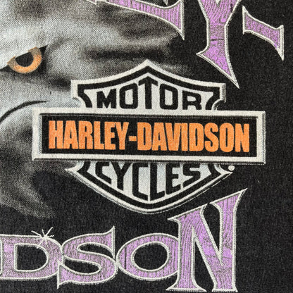 Harley-Davidson 2000's Eagle Black Tee features a boxy black T-shirt with a front graphic of an eagle's head alongside a Harley-Davidson logo. Purple and white “Harley Davidson” text and “Thunderstrikes” graphics surround the design. The back has a large white and grey graphic of a flying eagle with Harley-Davidson text underneath.

