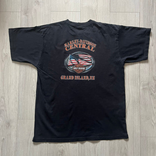  Harley Davidson Grand Island 2000’s Tee featuring a fiery Harley Davidson Motorcycles logo on the front and a USA flag graphic with Harley branding and “Grand Island, NE” text on the back. Classic black vintage tee with a timeless biker aesthetic.