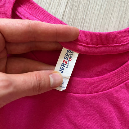 Hand holding a pink garment with a Jerzees tag on a light wooden surface