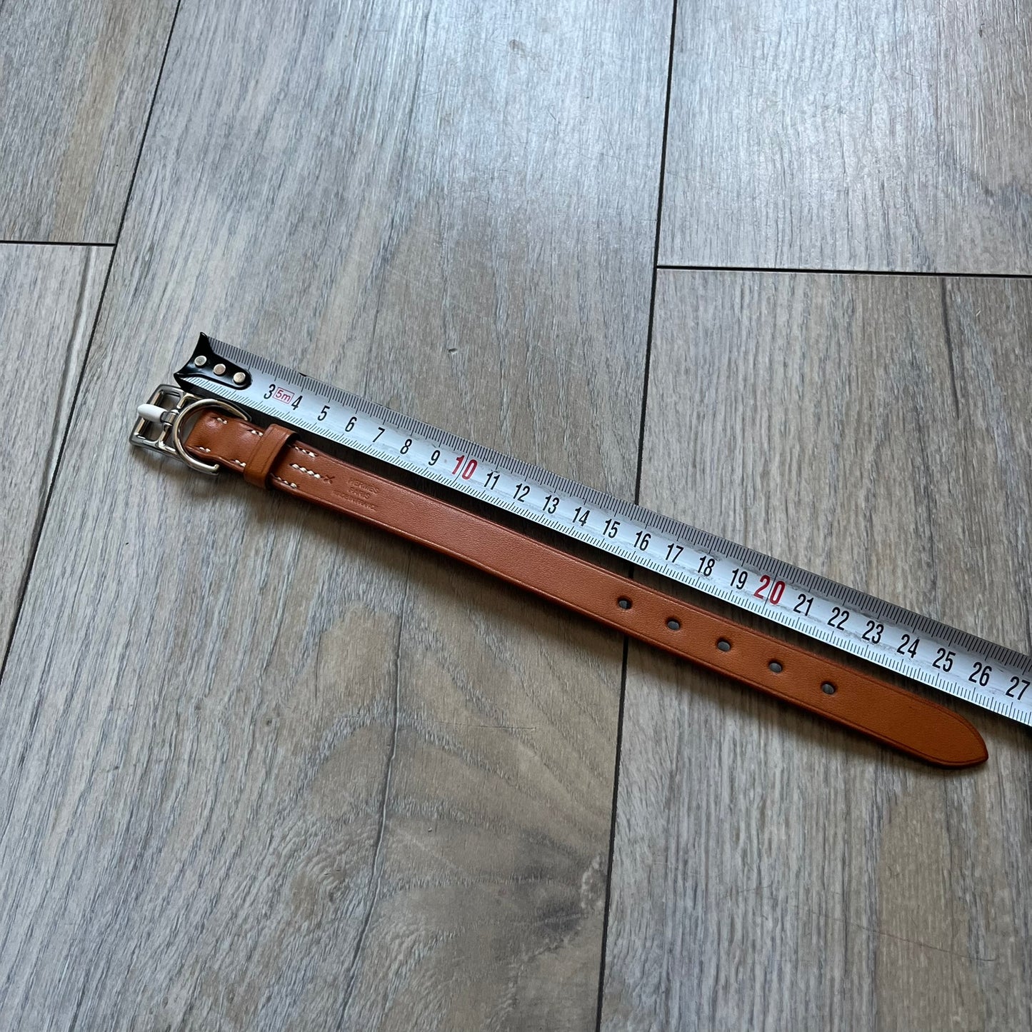 Small model Hermès Étrivière dog collar crafted from Natural Sable bridle leather. The collar features a stirrup-shaped buckle stamped HERMÈS, a metal D-ring for leash attachment, and leather stamped “HERMÈS PARIS MADE IN FRANCE.” It includes a 2 cm silver-plated stainless steel medal engraved “Hermès Sellier Paris,” with the reverse side suitable for engraving