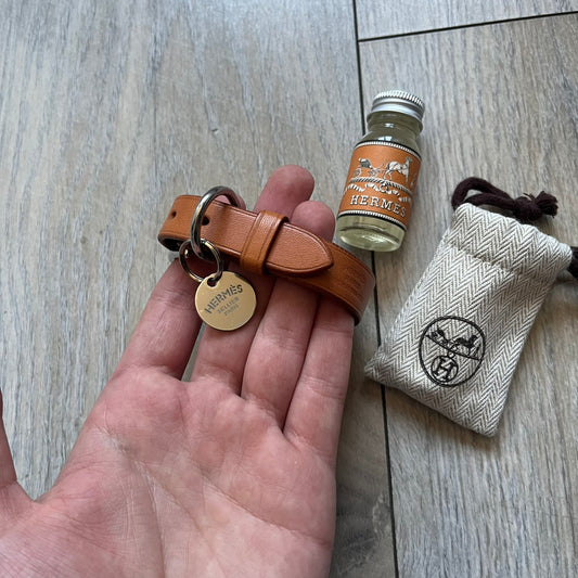 Small model Hermès Étrivière dog collar crafted from Natural Sable bridle leather. The collar features a stirrup-shaped buckle stamped HERMÈS, a metal D-ring for leash attachment, and leather stamped “HERMÈS PARIS MADE IN FRANCE.” It includes a 2 cm silver-plated stainless steel medal engraved “Hermès Sellier Paris,” with the reverse side suitable for engraving