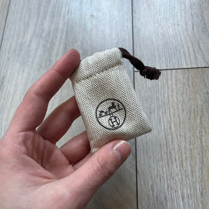 Small model Hermès Étrivière dog collar crafted from Natural Sable bridle leather. The collar features a stirrup-shaped buckle stamped HERMÈS, a metal D-ring for leash attachment, and leather stamped “HERMÈS PARIS MADE IN FRANCE.” It includes a 2 cm silver-plated stainless steel medal engraved “Hermès Sellier Paris,” with the reverse side suitable for engraving