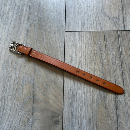 Small model Hermès Étrivière dog collar crafted from Natural Sable bridle leather. The collar features a stirrup-shaped buckle stamped HERMÈS, a metal D-ring for leash attachment, and leather stamped “HERMÈS PARIS MADE IN FRANCE.” It includes a 2 cm silver-plated stainless steel medal engraved “Hermès Sellier Paris,” with the reverse side suitable for engraving