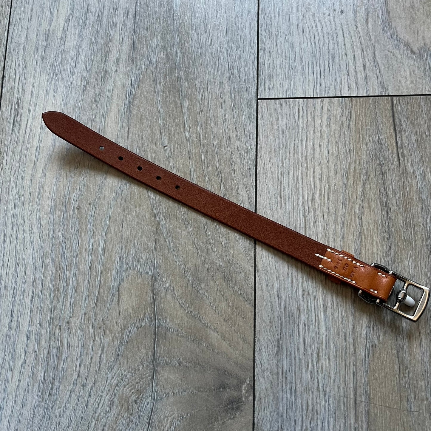 Small model Hermès Étrivière dog collar crafted from Natural Sable bridle leather. The collar features a stirrup-shaped buckle stamped HERMÈS, a metal D-ring for leash attachment, and leather stamped “HERMÈS PARIS MADE IN FRANCE.” It includes a 2 cm silver-plated stainless steel medal engraved “Hermès Sellier Paris,” with the reverse side suitable for engraving