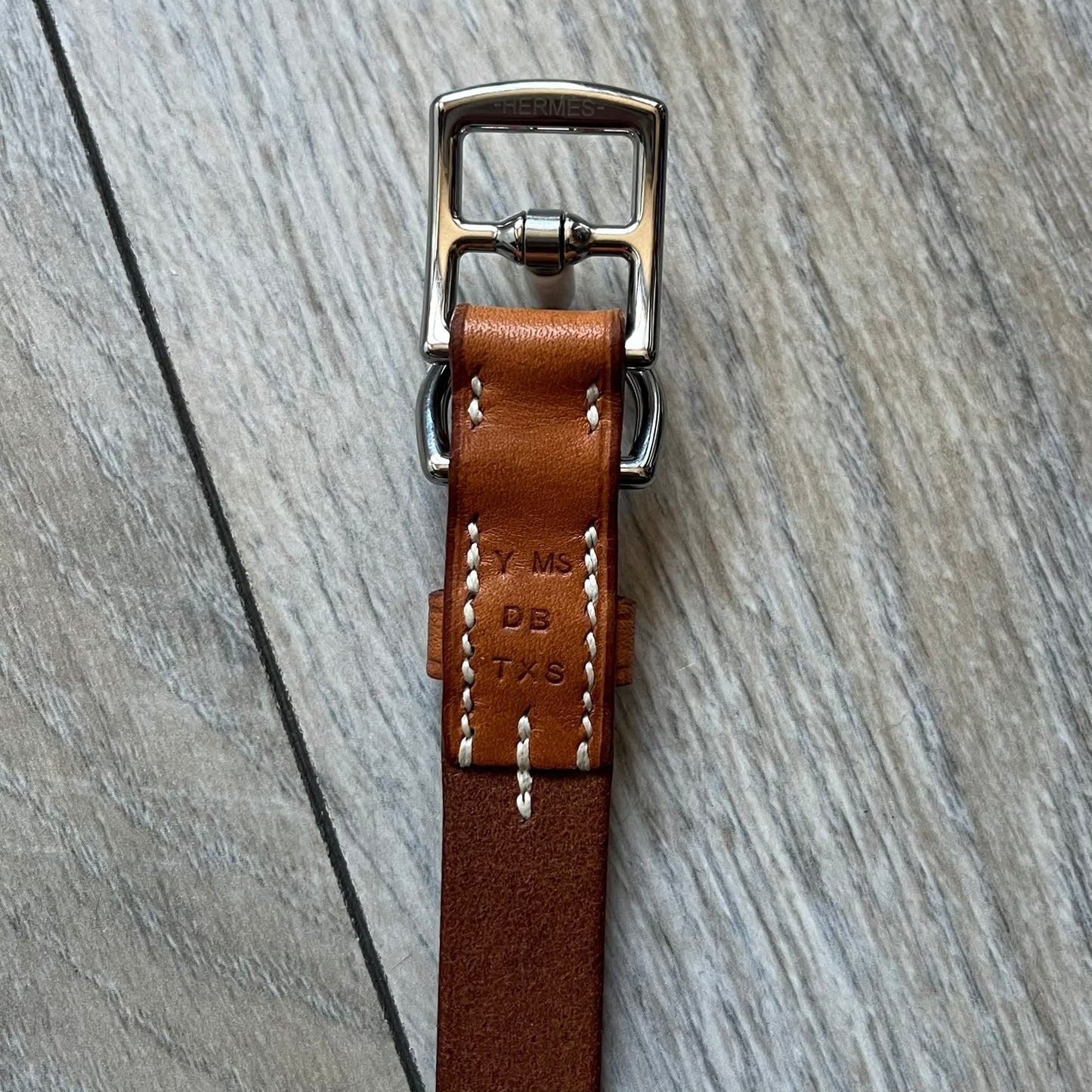 Small model Hermès Étrivière dog collar crafted from Natural Sable bridle leather. The collar features a stirrup-shaped buckle stamped HERMÈS, a metal D-ring for leash attachment, and leather stamped “HERMÈS PARIS MADE IN FRANCE.” It includes a 2 cm silver-plated stainless steel medal engraved “Hermès Sellier Paris,” with the reverse side suitable for engraving