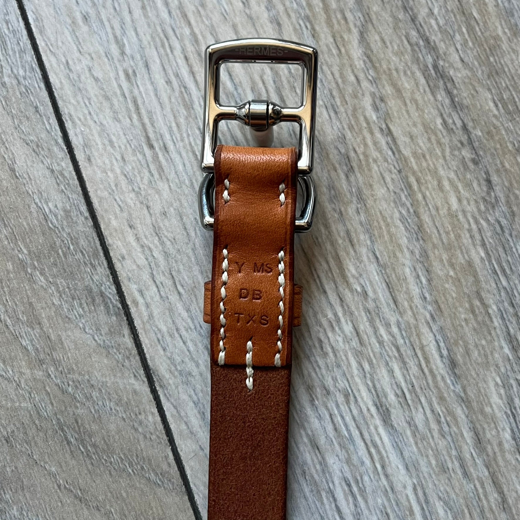 Small model Hermès Étrivière dog collar crafted from Natural Sable bridle leather. The collar features a stirrup-shaped buckle stamped HERMÈS, a metal D-ring for leash attachment, and leather stamped “HERMÈS PARIS MADE IN FRANCE.” It includes a 2 cm silver-plated stainless steel medal engraved “Hermès Sellier Paris,” with the reverse side suitable for engraving