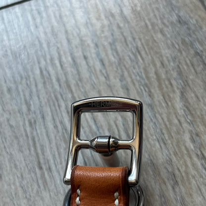 Small model Hermès Étrivière dog collar crafted from Natural Sable bridle leather. The collar features a stirrup-shaped buckle stamped HERMÈS, a metal D-ring for leash attachment, and leather stamped “HERMÈS PARIS MADE IN FRANCE.” It includes a 2 cm silver-plated stainless steel medal engraved “Hermès Sellier Paris,” with the reverse side suitable for engraving