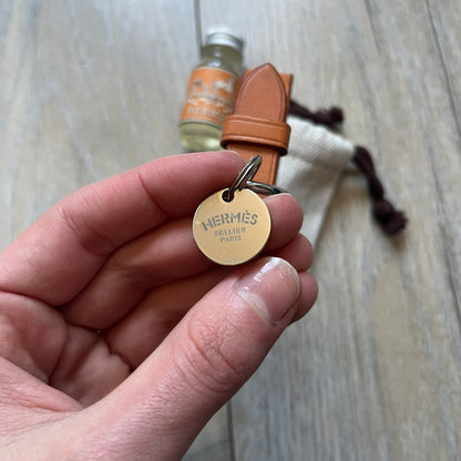 Small model Hermès Étrivière dog collar crafted from Natural Sable bridle leather. The collar features a stirrup-shaped buckle stamped HERMÈS, a metal D-ring for leash attachment, and leather stamped “HERMÈS PARIS MADE IN FRANCE.” It includes a 2 cm silver-plated stainless steel medal engraved “Hermès Sellier Paris,” with the reverse side suitable for engraving