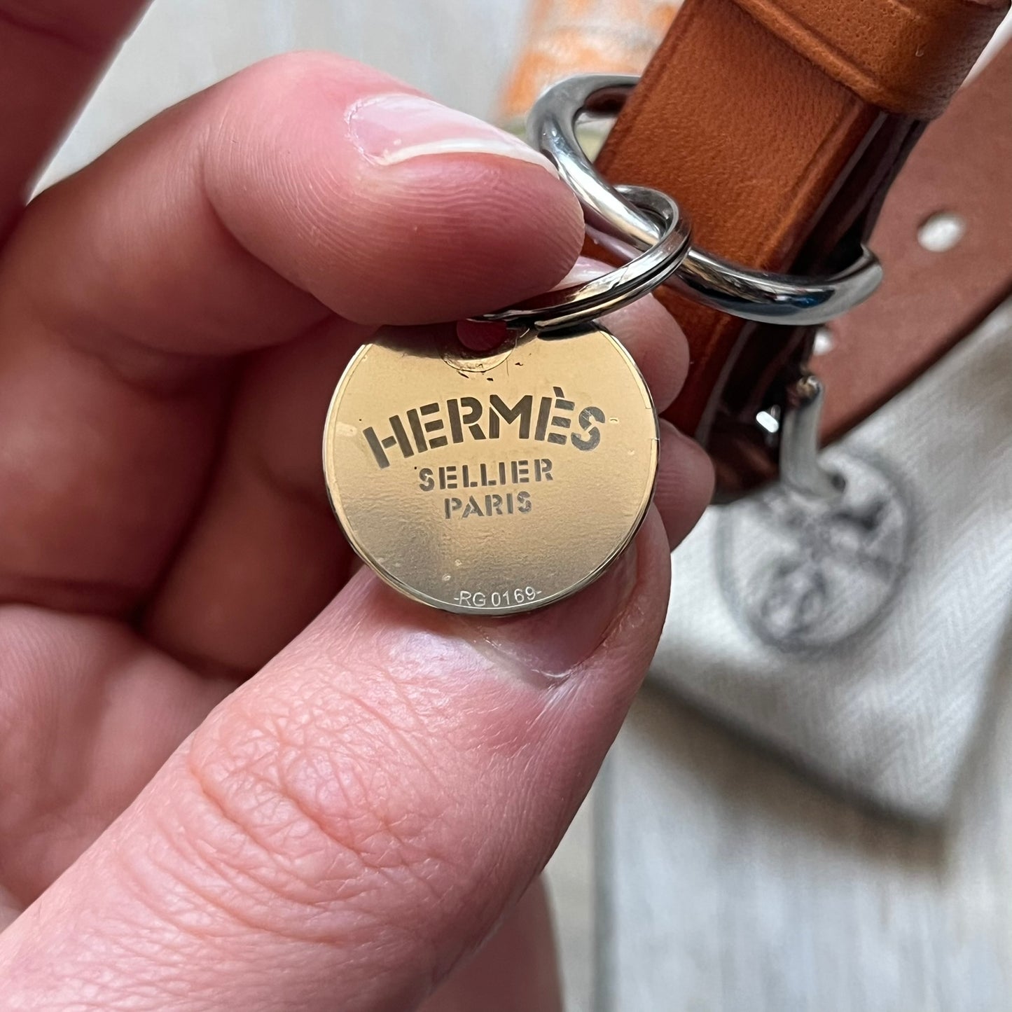 Small model Hermès Étrivière dog collar crafted from Natural Sable bridle leather. The collar features a stirrup-shaped buckle stamped HERMÈS, a metal D-ring for leash attachment, and leather stamped “HERMÈS PARIS MADE IN FRANCE.” It includes a 2 cm silver-plated stainless steel medal engraved “Hermès Sellier Paris,” with the reverse side suitable for engraving